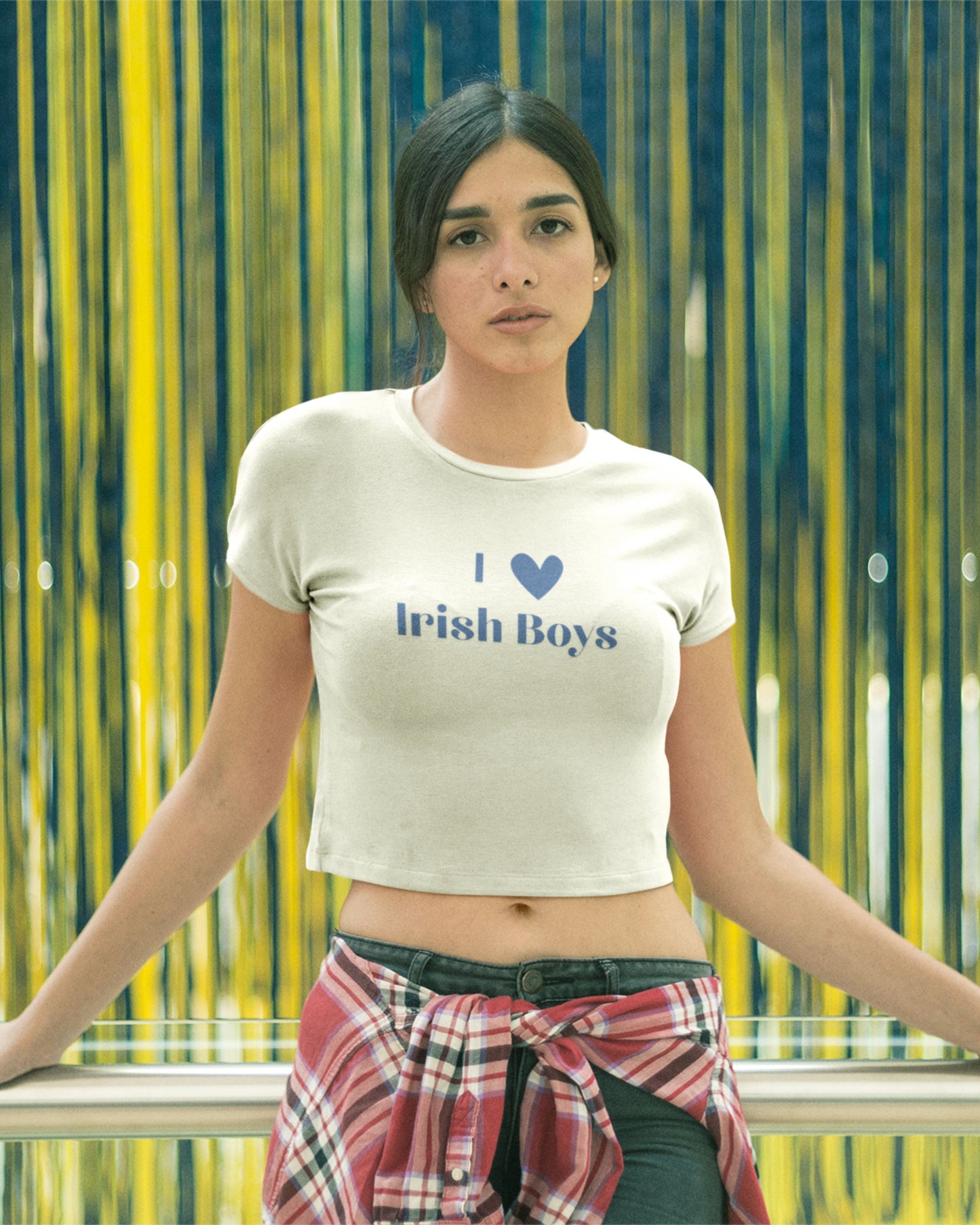 Young girl leaning on railing at party wearing a I love Irish boys crop top. The party is for St. Patricks day. She is also wearing jeans and flannel on waist.