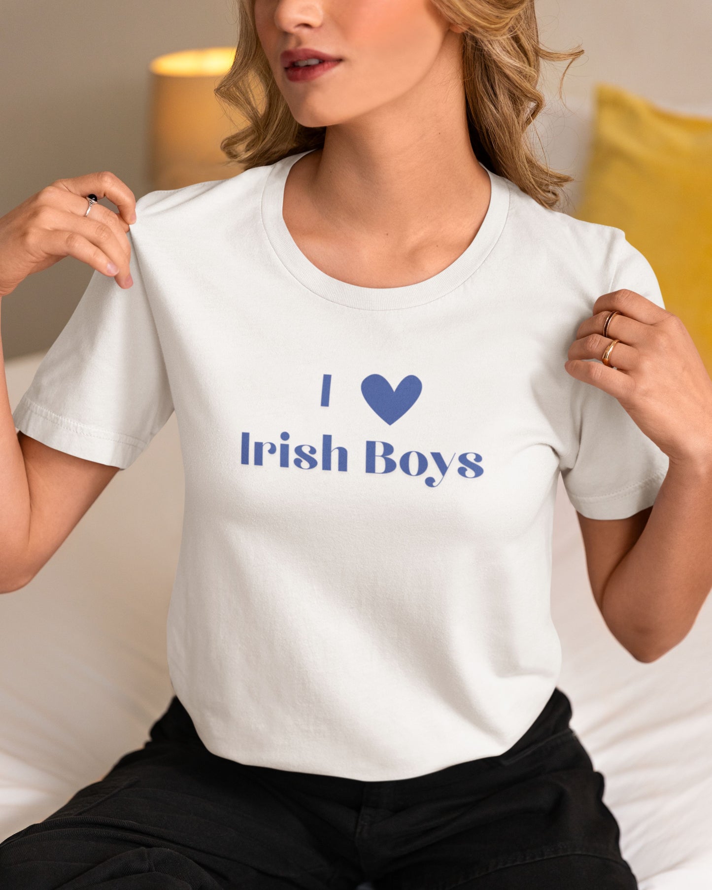 Blonde women showing off her I Love Irish Boys T-Shirt. She is sitting on her bed and hearing black pants.
